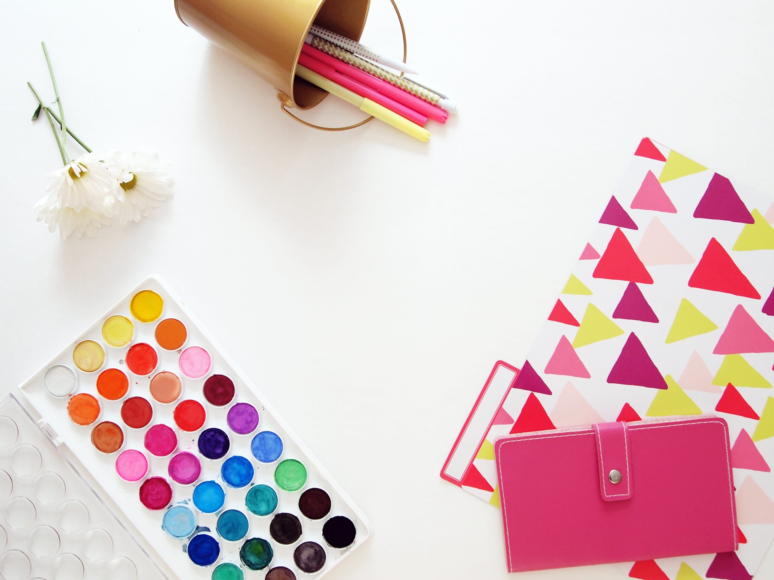 watercolor paint, a folder, pens, and a wallet on a white table
