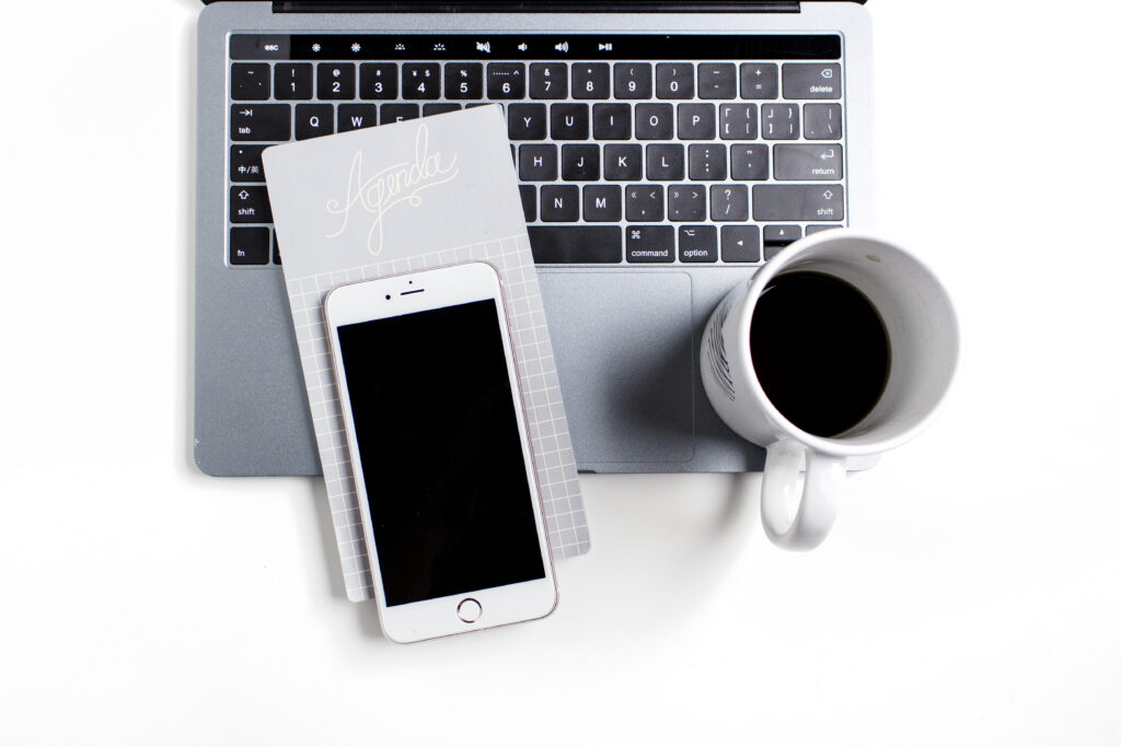 mug of coffee, cell phone, and agenda list beside a laptop