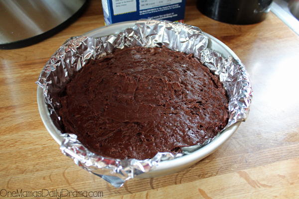 A round cake pan lined with aluminum foil and filled with chocolate batter.