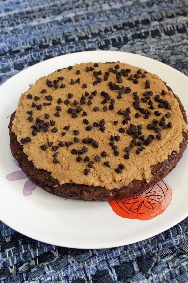 A round chocolate brownie frosted with peanut butter cream cheese and sprinkled with chocolate chips.