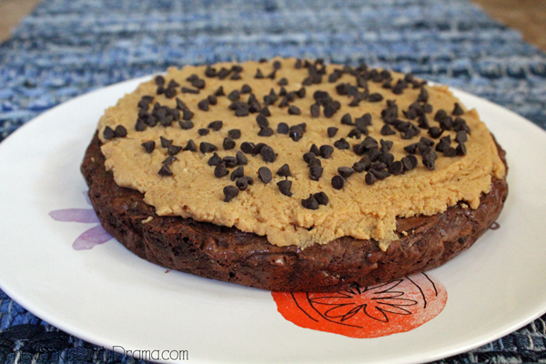 A round chocolate brownie frosted with peanut butter cream cheese and sprinkled with chocolate chips.
