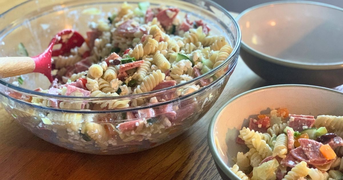 A bowl of Greek pasta salad with rotini, salami, feta, and vegetables.