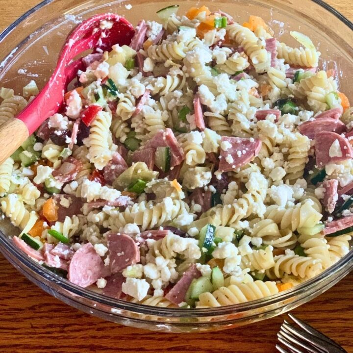 Greek pasta salad with rotini, feta, salami, cucumber, tomato, onion, olives, and bell peppers.