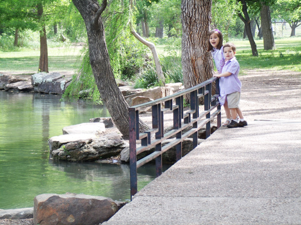 two kids stand on a bridge looking into a pond at the Fort Worth Botanic Garden