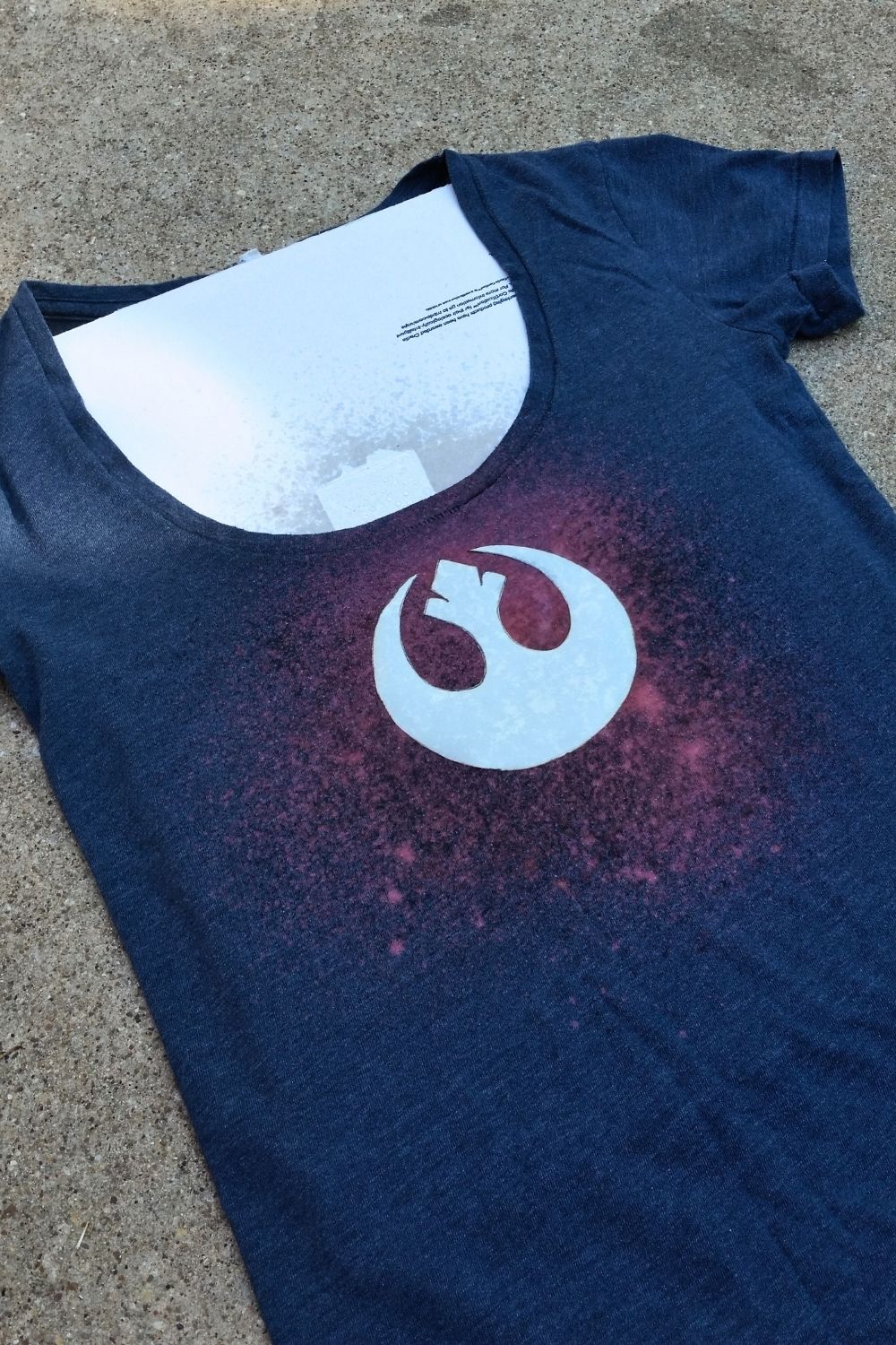 A navy shirt with pink bleach splatters in the center around a stencil.