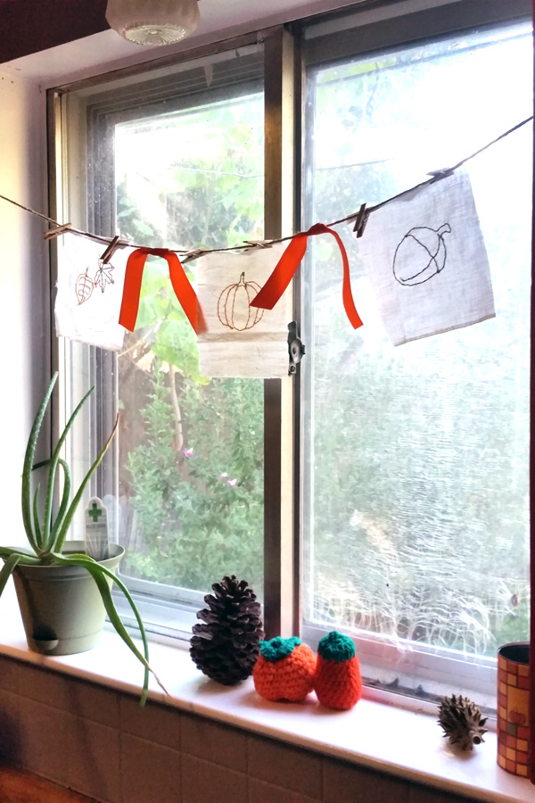 fall bunting hanging in a window above an aloe vera plant, pinecones, and crocheted pumpkins