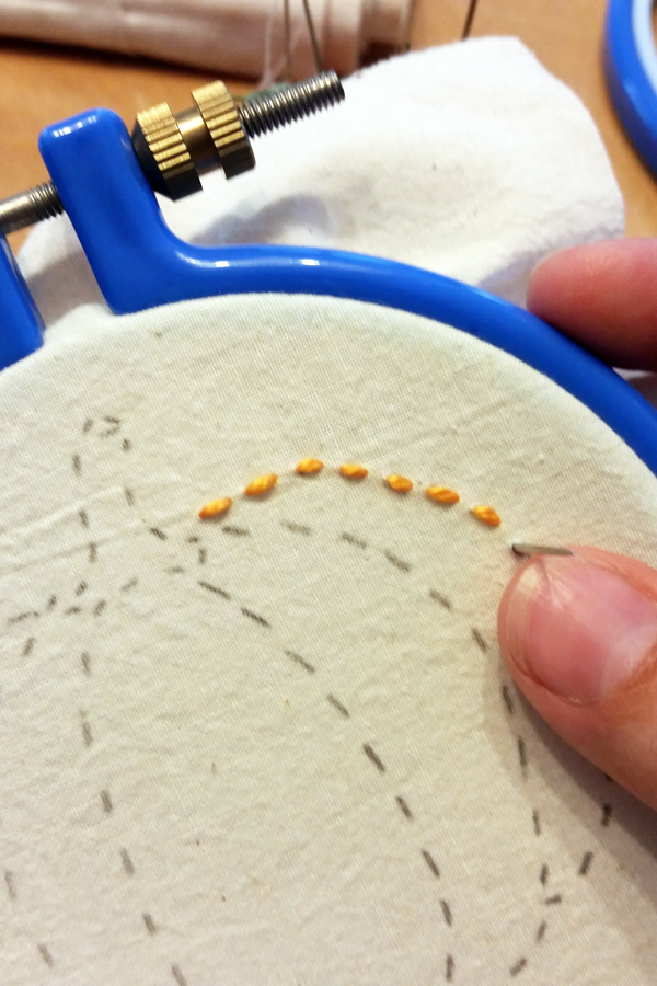 hand stitching orange thread onto a pumpkin pattern