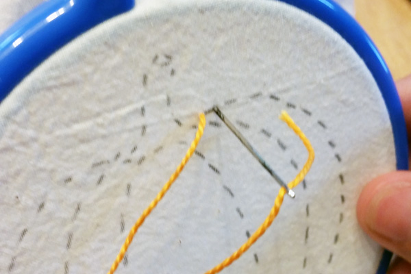 hand stitching orange thread along the lines of the pumpkin pattern