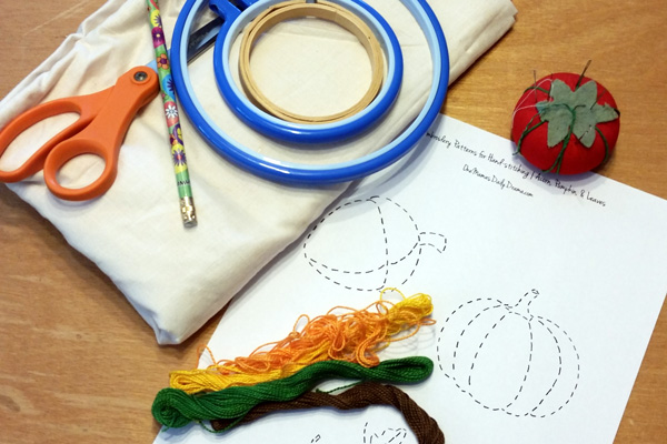embroidery hoop, thread, scissors, fabric, pincushion with needles, and paper pattern
