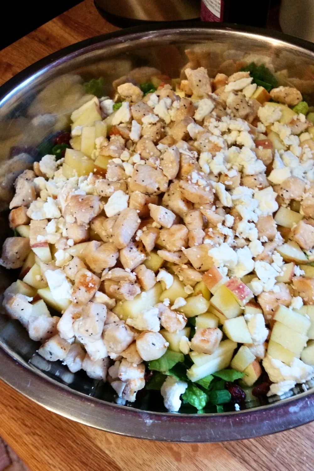 Cooked chicken, feta, and apples on top of a bowl of romaine lettuce.