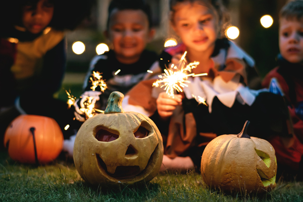 carved jack-o-lanterns at dusk and kids with sparklers out of focus in the background