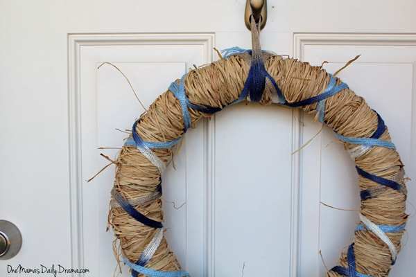 A ribbon and raffia wreath hanging on a white door from a metal Command hook.