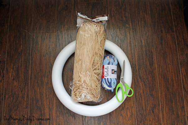 A white foam wreath form, a bag of natural raffia, a roll of blue yarn, and a pair of scissors.