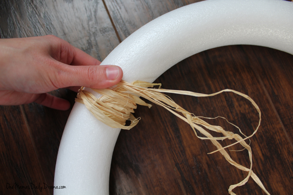 A hand wrapping raffia around a white foam wreath form.