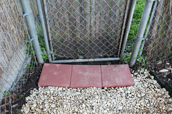 White gravel filling in a path up to a chain link fence and red pavers.