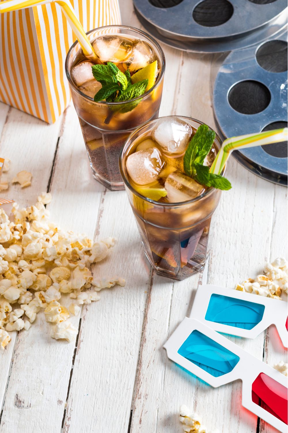 Two glasses of tea beside a box of popcorn and red-blue 3D movie glasses.