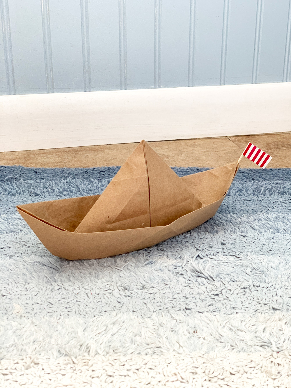 Brown paper origami boat sailing on a blue rug.