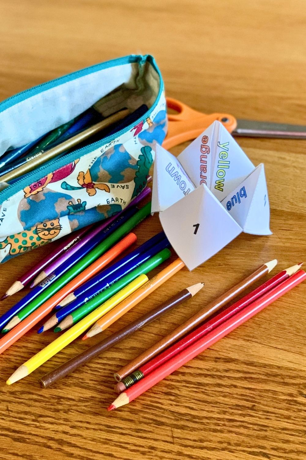 A paper cootie catcher beside a bag of colored pencils.