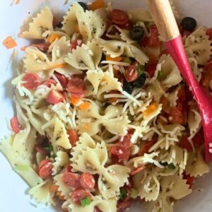 A bowl of pizza pasta salad with pepperoni, mozzarella, peppers, onion, tomato, and farfalle.