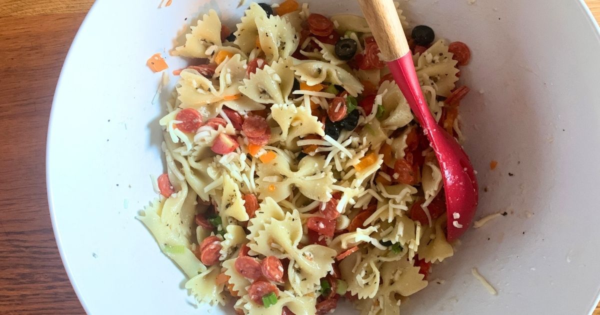 A bowl of pizza pasta salad with pepperoni, mozzarella, peppers, onion, tomato, and farfalle.