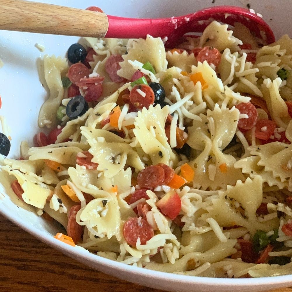 A bowl of pizza pasta salad with pepperoni, mozzarella, peppers, onion, tomato, and farfalle.