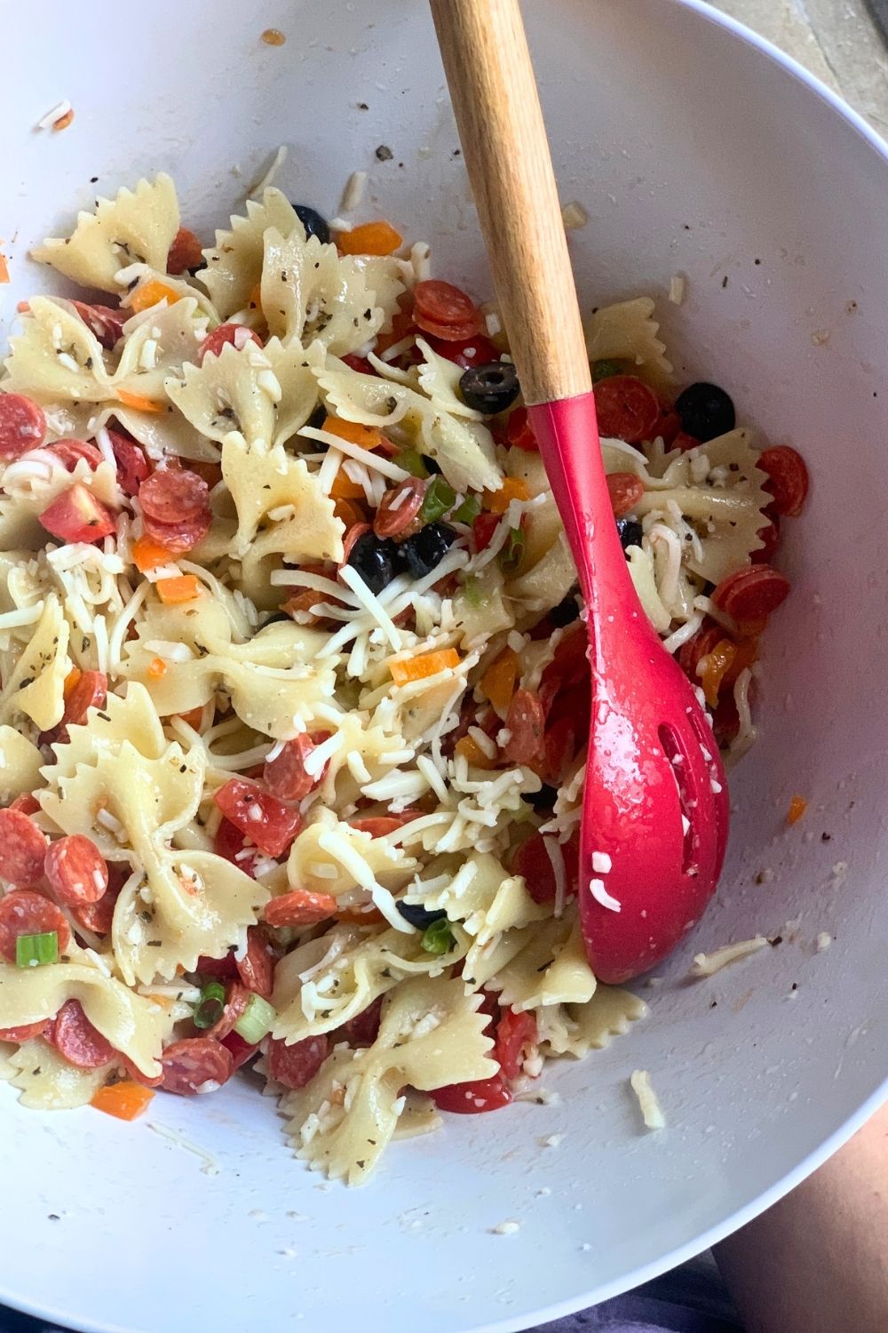 A bowl of pizza pasta salad with pepperoni, mozzarella, peppers, onion, tomato, and farfalle.