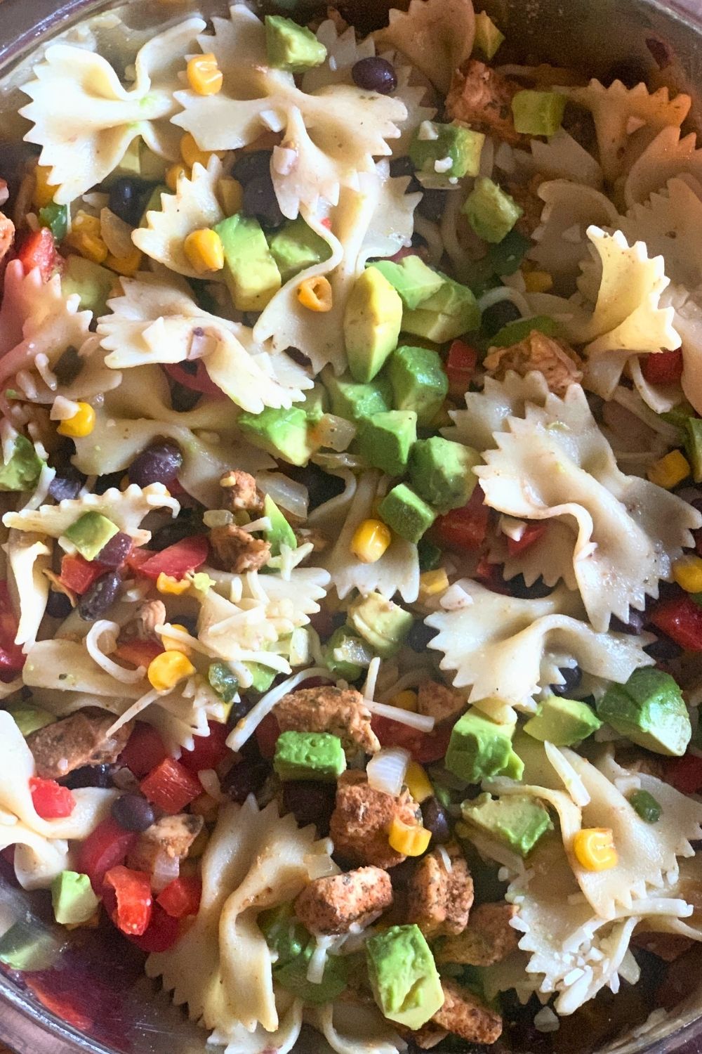 Closeup of bowl showing farfalle pasta, seasoned chicken, and green avocado chunks.