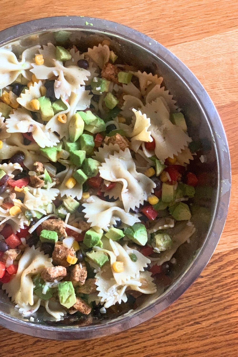 A bowl of pasta salad made with chicken, farfalle, avocado, tomato, onion, peppers, and black beans.