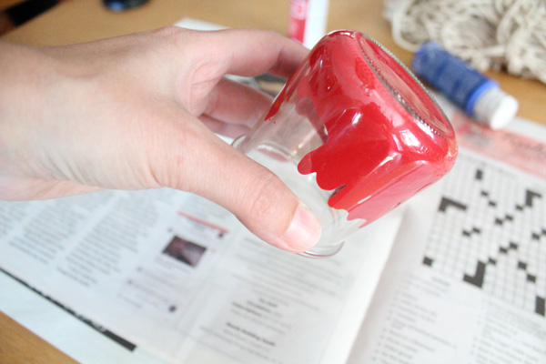 A hand turning a glass jar upside down to make red paint run up the sides.