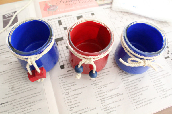 A trio of painted glass jars in red and blue with cotton cord and bead decoration.