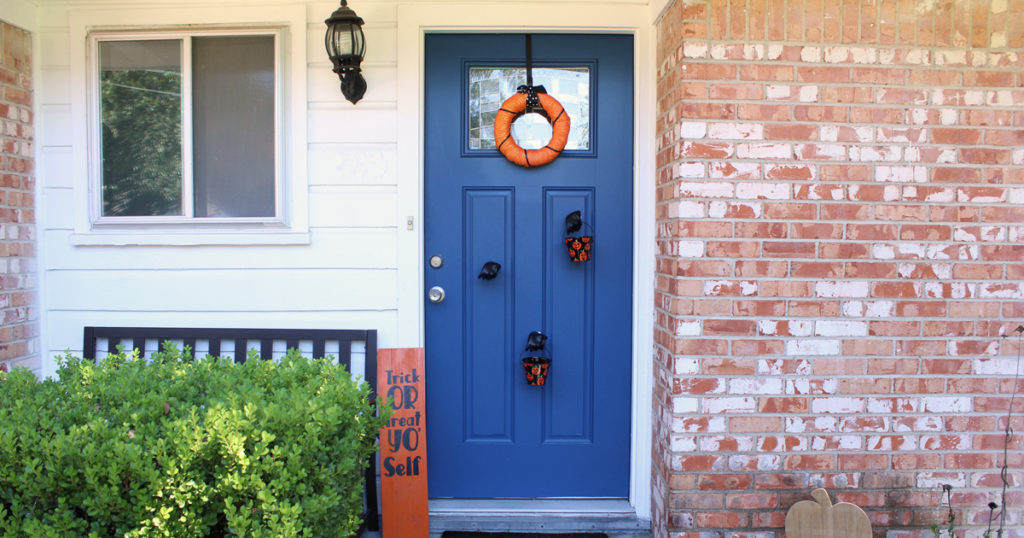 Black and orange Halloween porch / wreath, sign, and buckets of candy held by mannequin hands