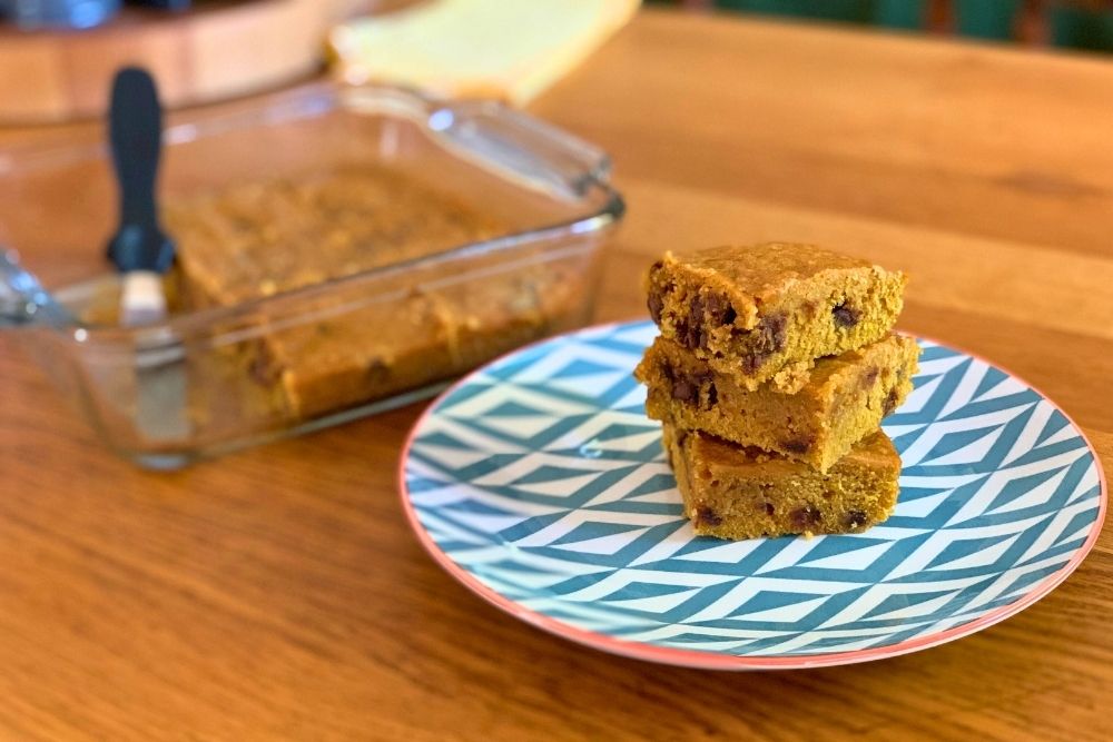 A stack of 3 pumpkin chocolate chip bars on a plate beside a glass pan.