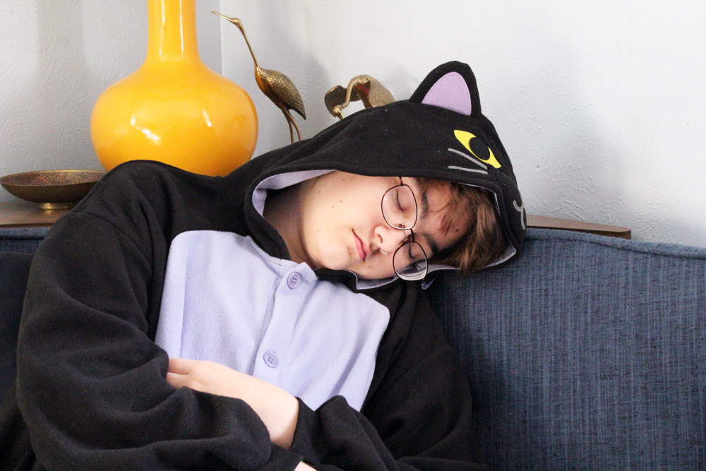 child wearing a black cat kigurumi and sleeping on a sofa