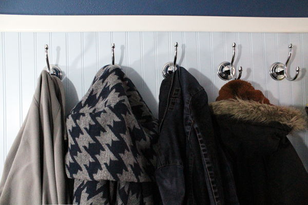 Four coats hang on chrome hooks against a blue paneled wall.