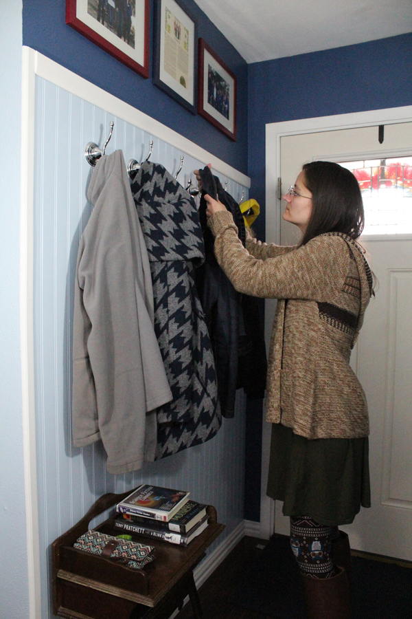 A woman hangs a coat on a hook against an entryway wall.