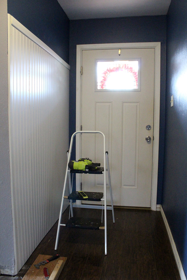 Entryway under construction with paneling on one wall. A latter and a nail gun sit in the middle.