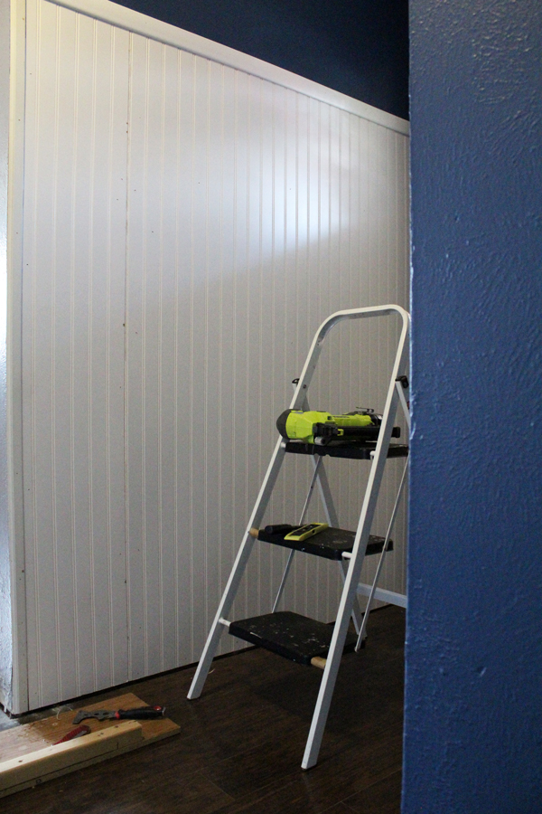 Small ladder in an entryway with paneling on the wall behind it.