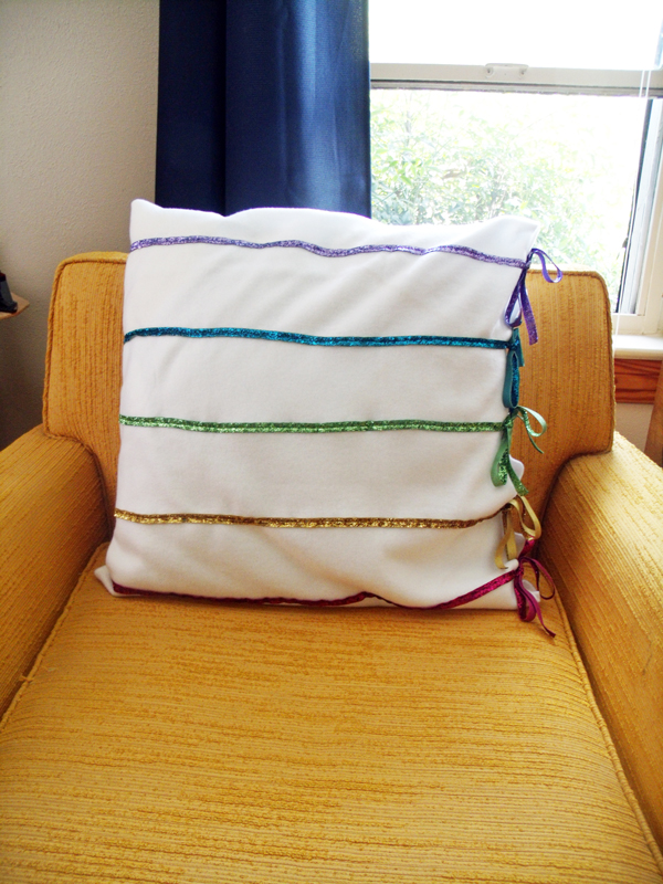 DIY rainbow ribbon pillow sitting in a yellow armchair in front of an open window