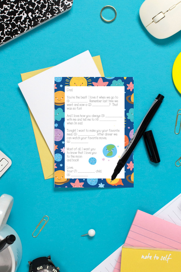 Father's Day card with a cartoon space theme on a blue table with a pen and other office supplies