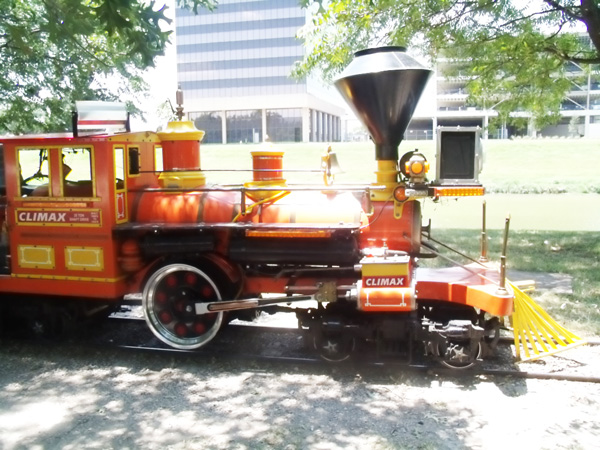a red engine in the Forest Park Miniature Railroad runs along a small track