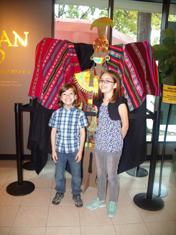 2 kids stand in front of a Peruvian gold display at the Irving Art Center