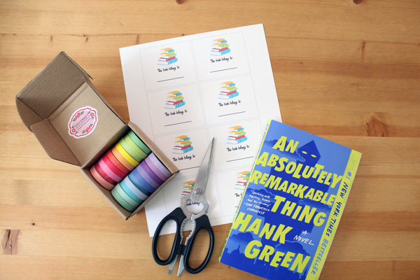 printed bookplates, washi tape, scissors, and a book on a pine countertop