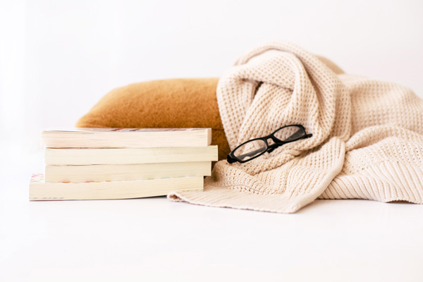 stack of paperback books beside a pillow and blanket