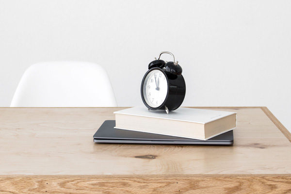 small clock sitting on top of 2 books on a wooden table
