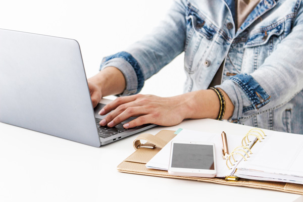 person in a denim jacked typing on a laptop beside an open planner