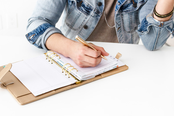 person in a denim jacket writing in a planner
