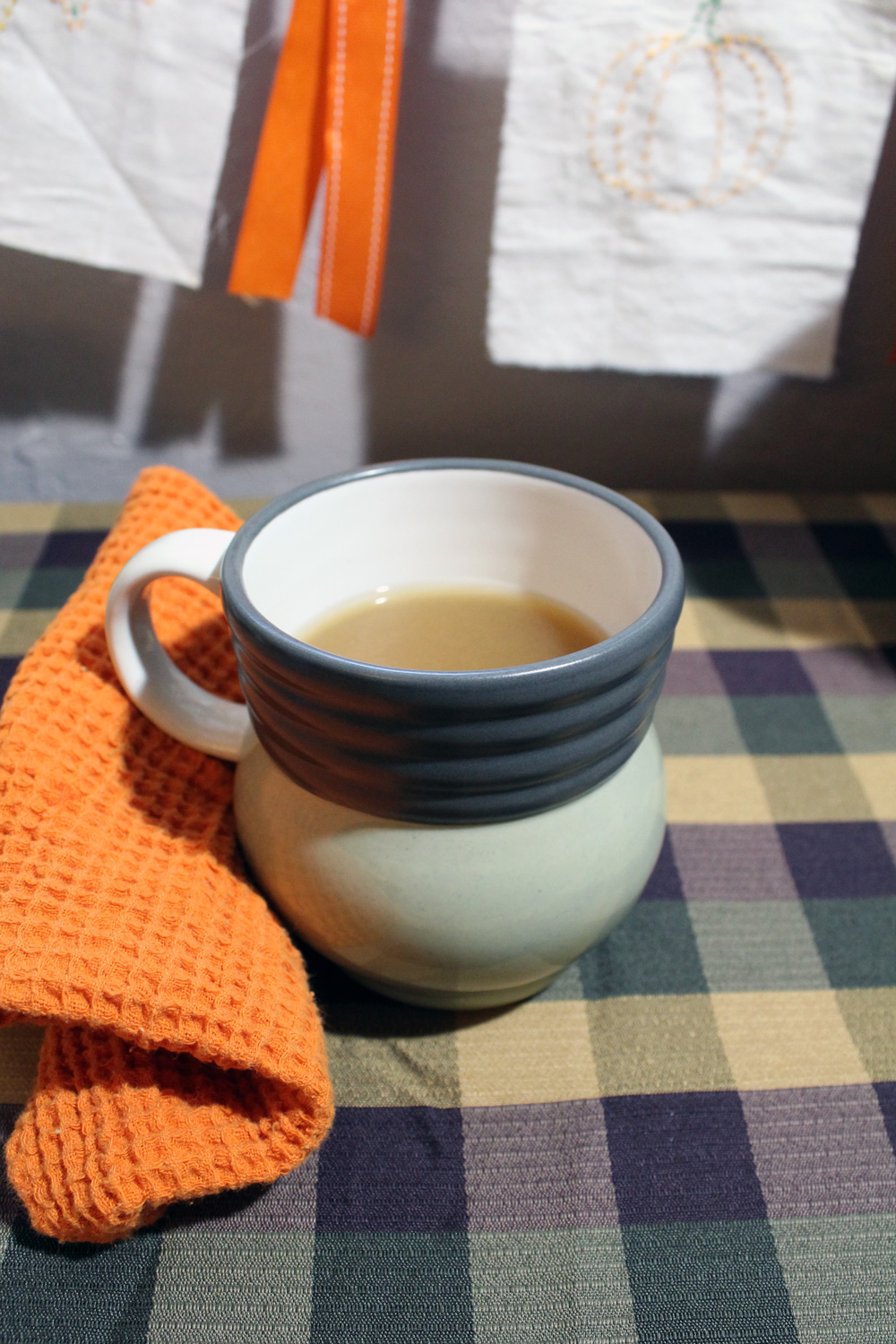 mug of warm cider on a green tablecloth with an orange dish towel