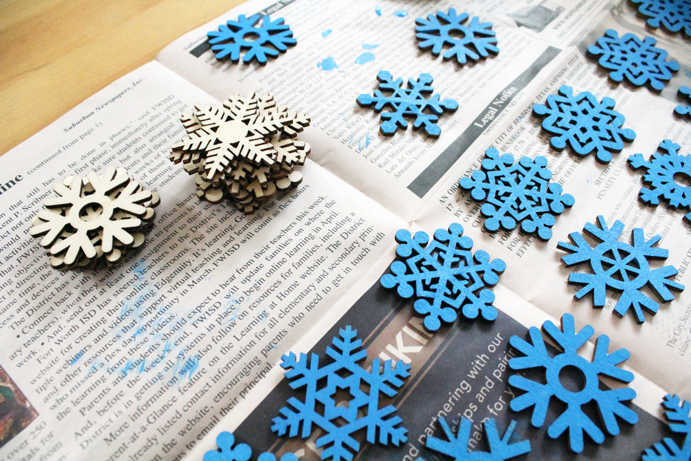 wooden snowflake cutouts stacked beside some blue painted snowflakes