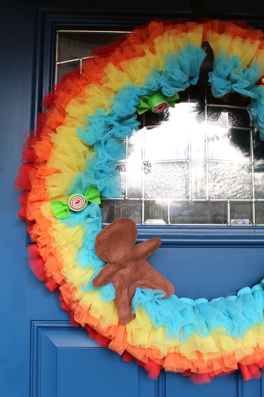 closeup of rainbow wreath with a felt gingerbread man in one corner and felt candies sprinkled around