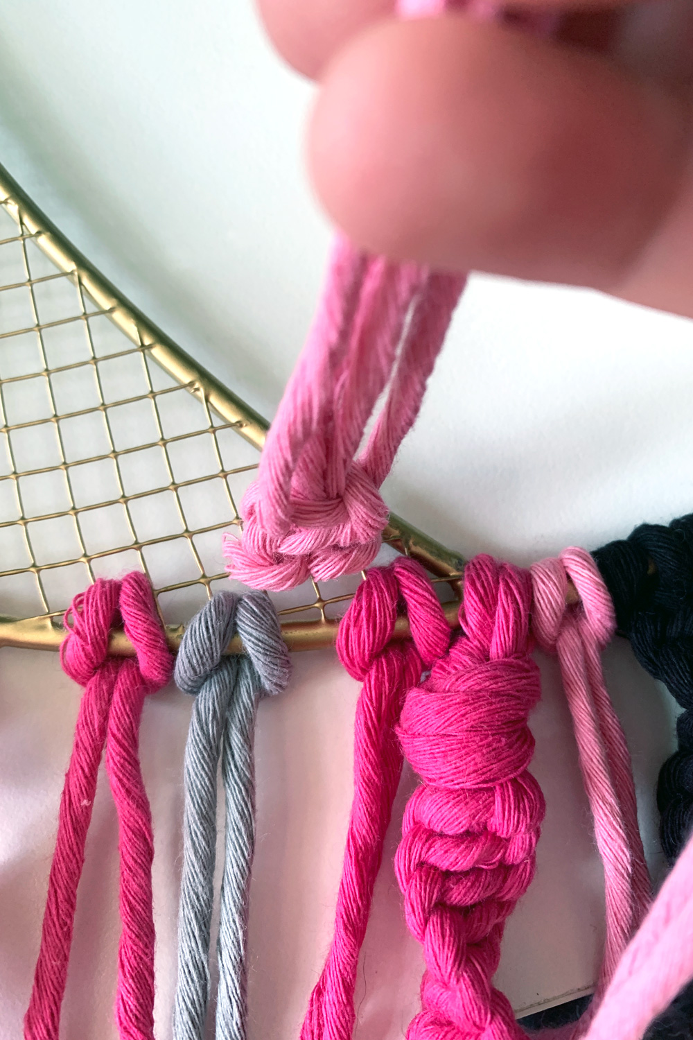 Several macrame cords and knots hanging from a wreath and overlapping one another.